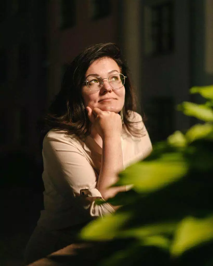 a woman with glasses sitting in front of a plant