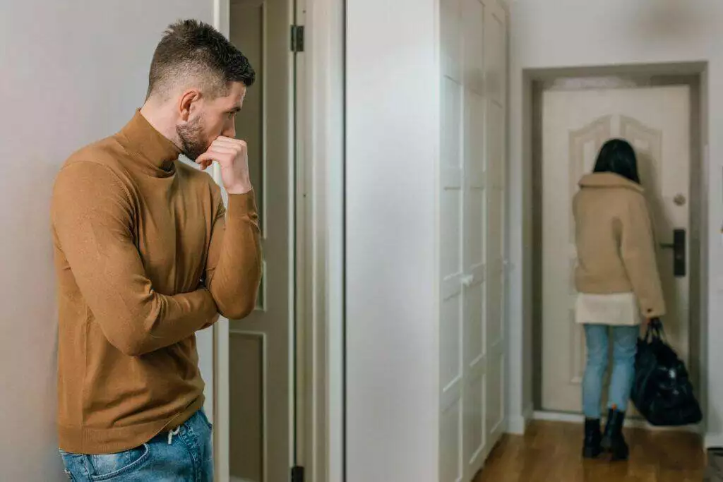 A couple experiencing a tense moment as a woman walks out of the apartment.