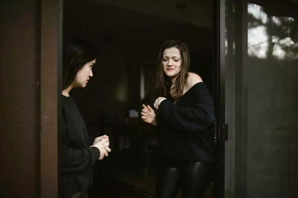 Two women in an emotional conversation at a doorway, highlighting tension.