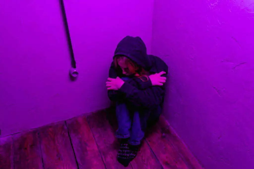 A teenager sits alone in a purple-lit corner, depicting solitude.