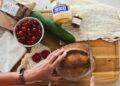 Person cutting bread on cutting board with groceries scattered on the table (Unsplash | Grace O'Driscoll)