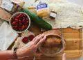 Person cutting bread on cutting board with groceries scattered on the table (Unsplash | Grace O'Driscoll)