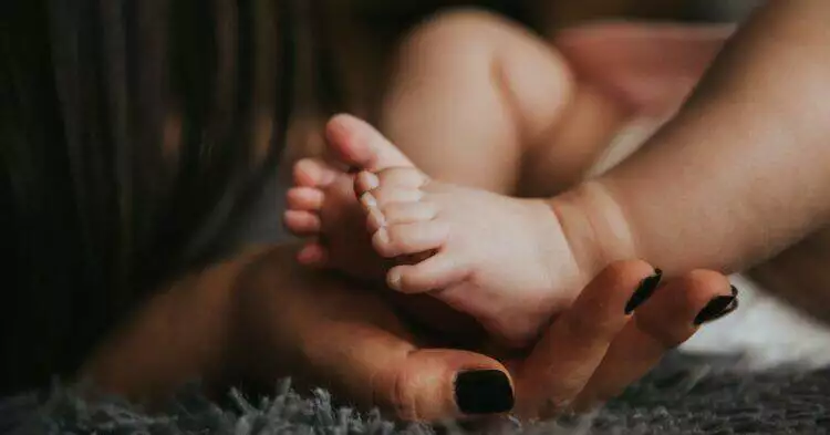 Mother holding baby's feet (Unsplash | Alex Pasarelu)