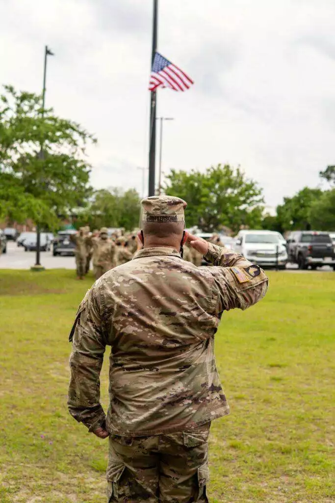 A soldier salutes the American flag at half mast during a ceremony outside.