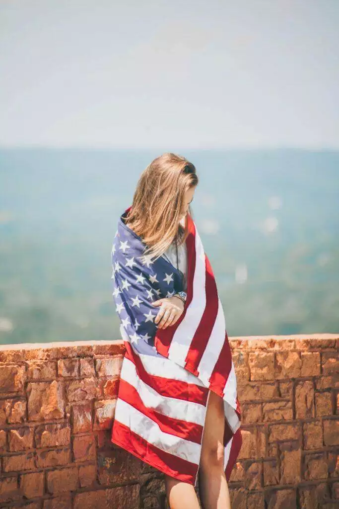 woman standing leaning on brick wall wrapping body with U.S. flag near body of water