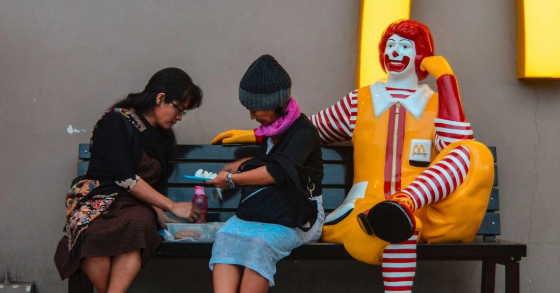 People eating next to McDonald's clown on bench