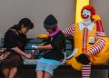 People eating next to McDonald's clown on bench