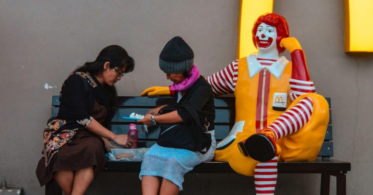 People eating next to McDonald's clown on bench