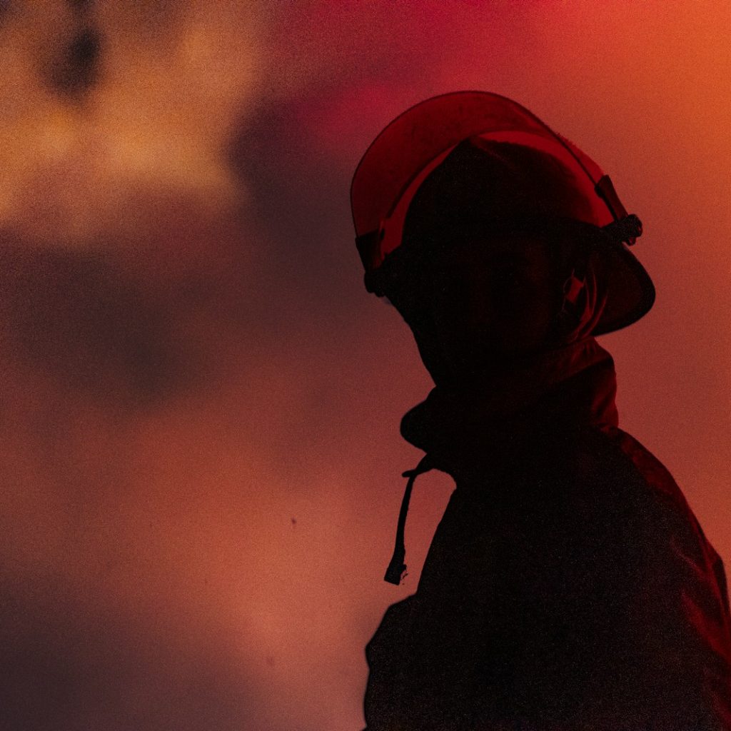 A firefighter stands in front of a fiery sky.