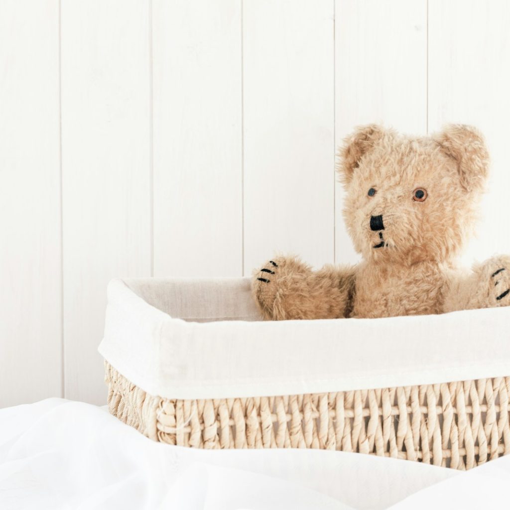 a teddy bear sitting in a basket on a bed