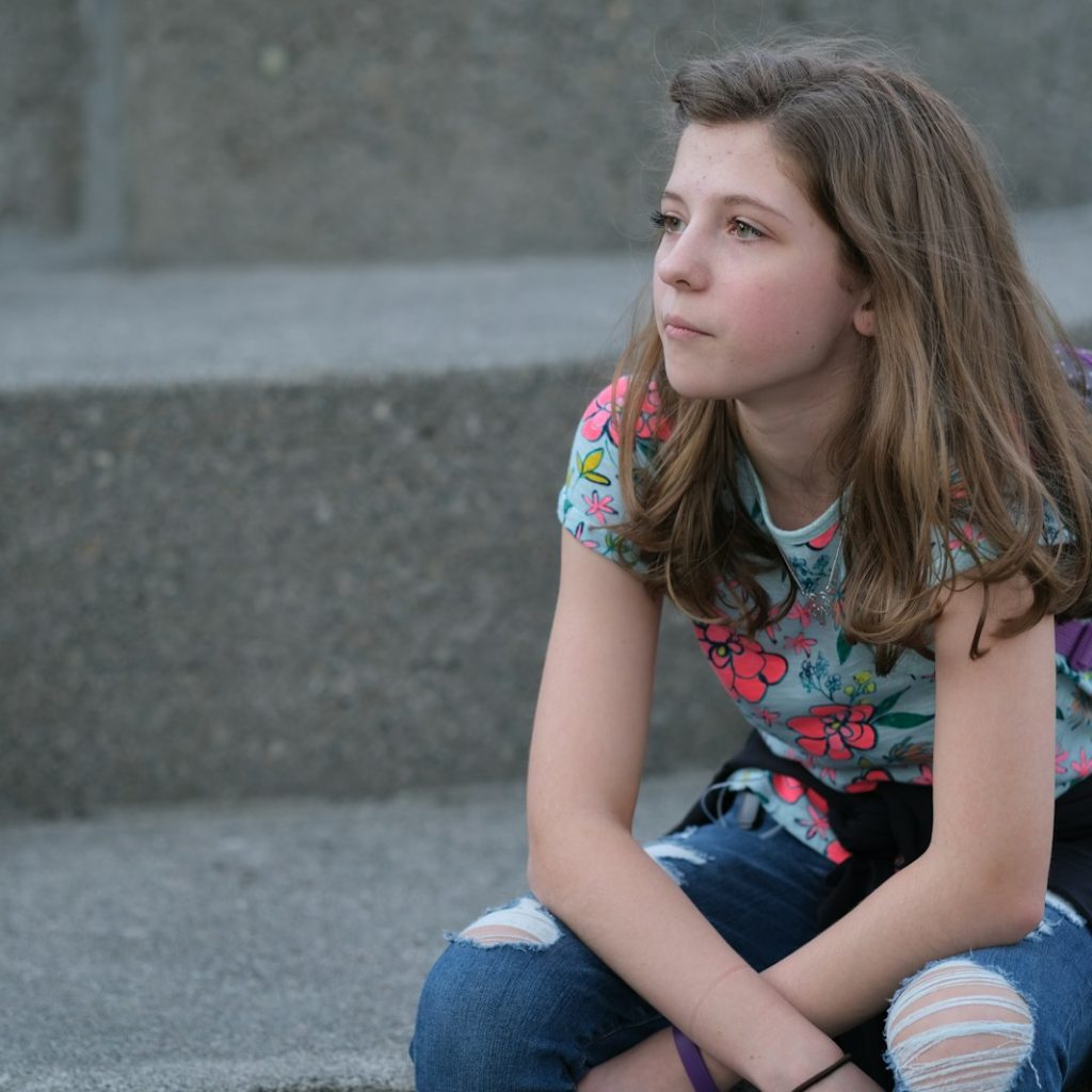 A young girl sitting on steps with a backpack on